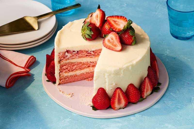 A strawberry layer cake with a cut slice showing pink cake layers